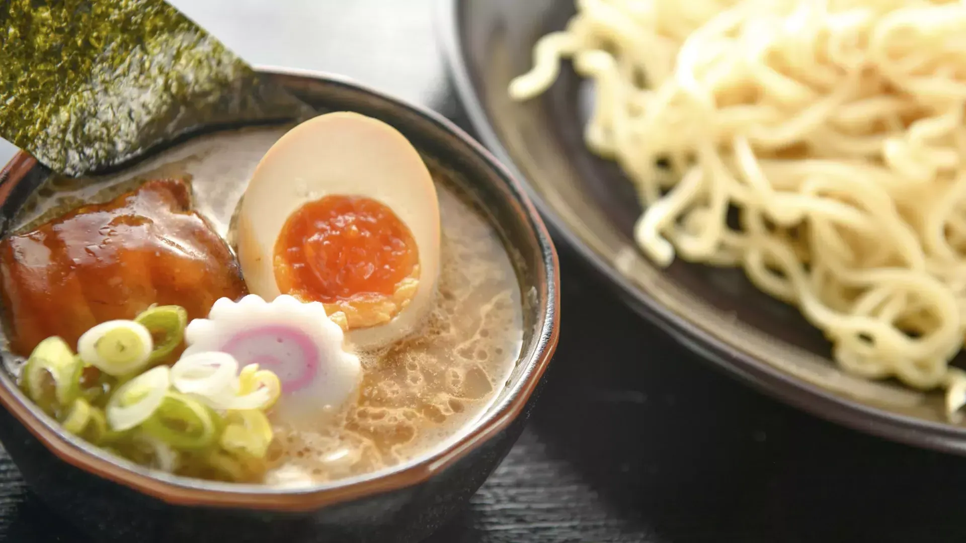 Gros plan d'un bol de nouilles et d'un bol de soupe ramen avec un œuf poché, coupé en deux.